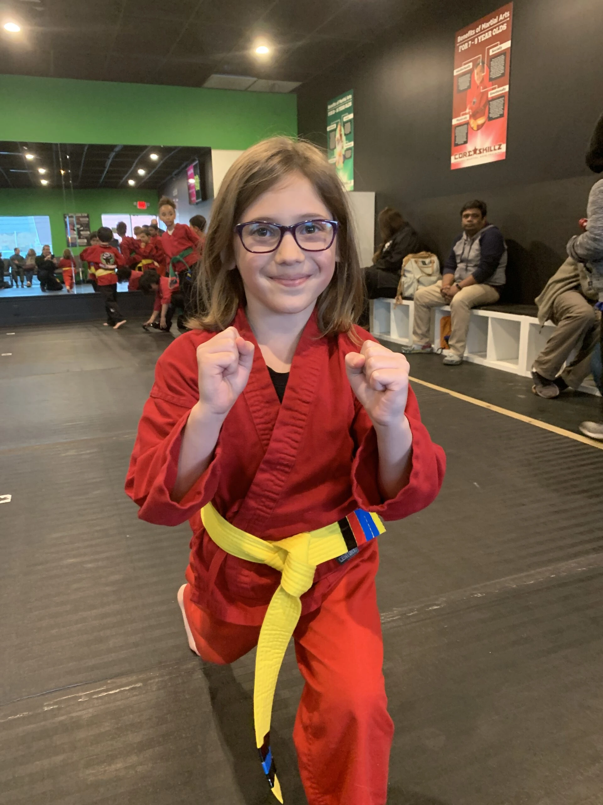 a girl with glasses, smiling, in a karate pose.