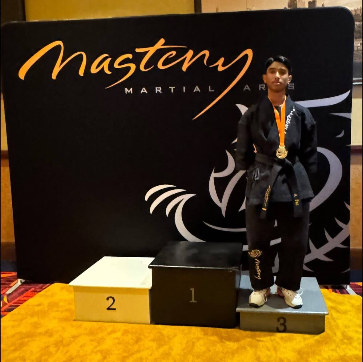Anay standing on podium with medal as a Black Belt.