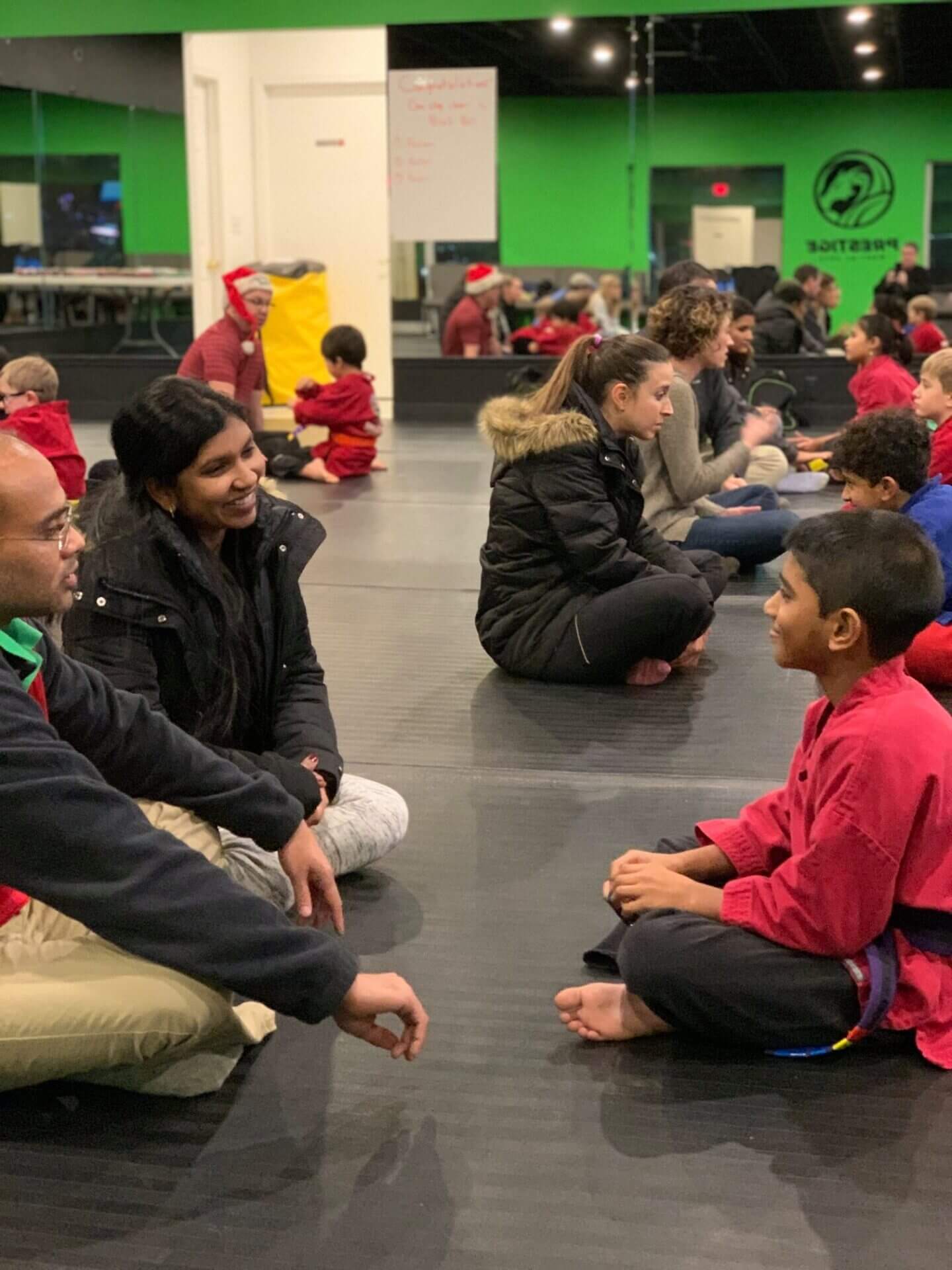 Anay sitting with mom and dad in karate class.